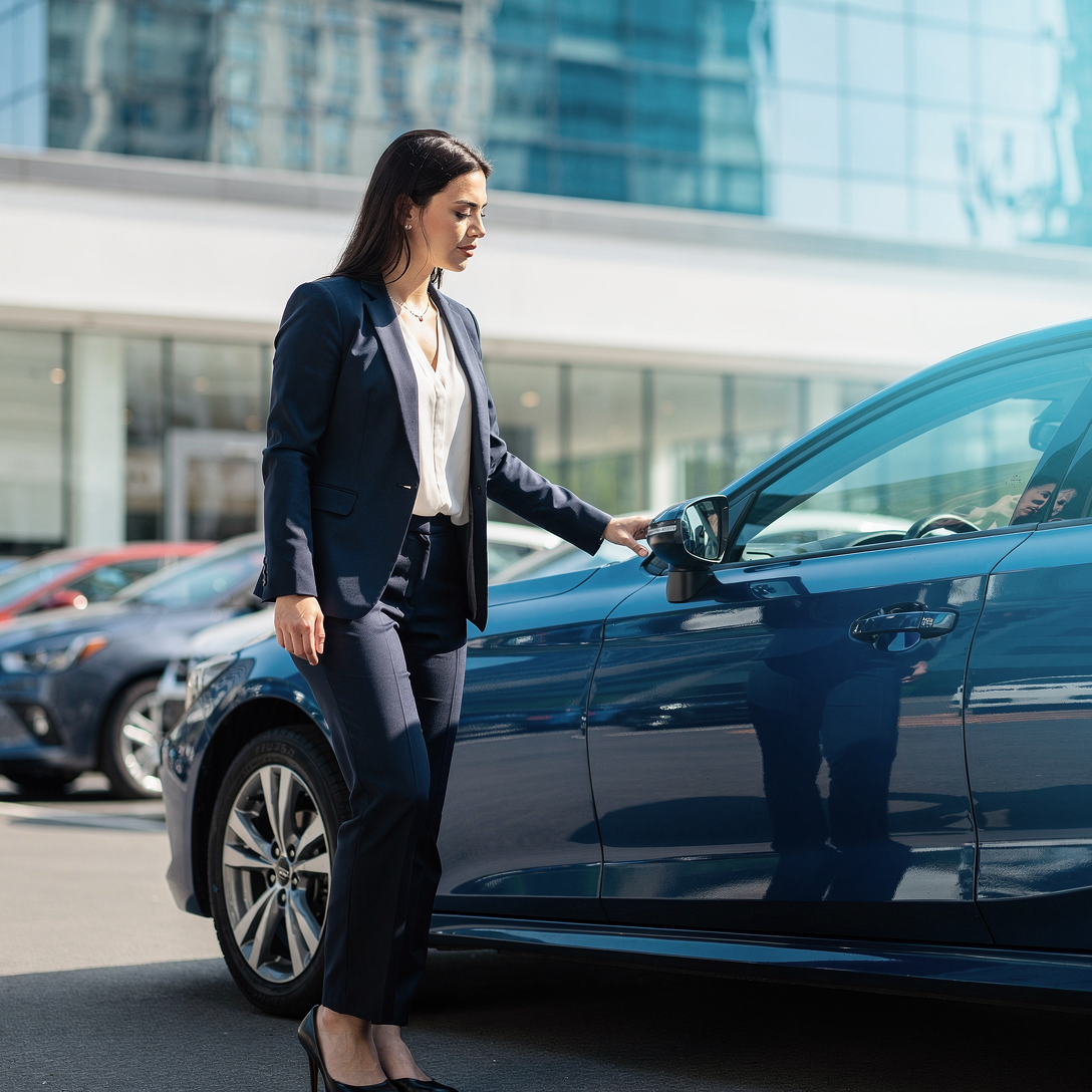 Woman in a business suit contemplating a blue car at a used car dealership